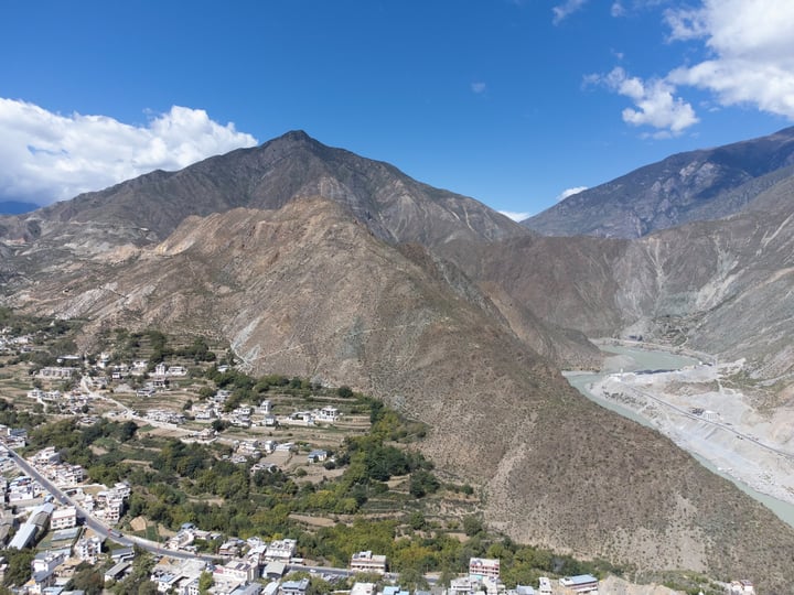 A mountainous valley with a small town nestled between mountains, surrounded by lush greenery and a river.