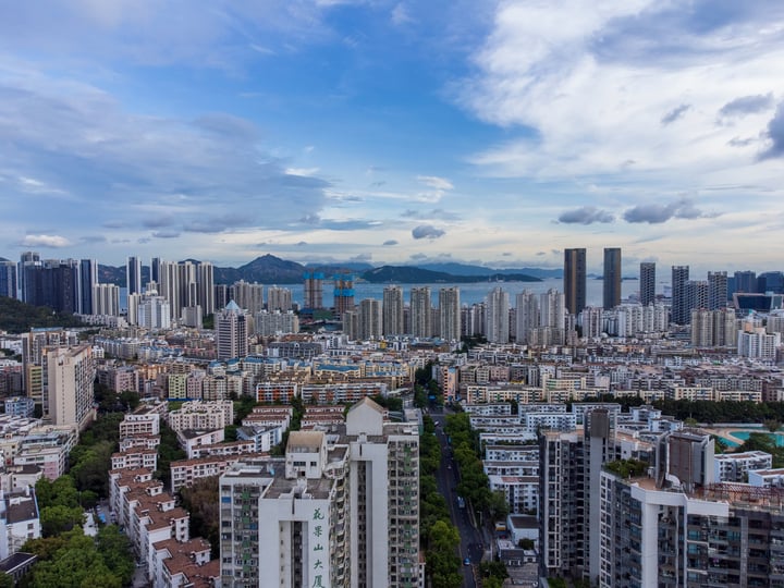 A panoramic view of a bustling city with tall buildings, a large body of water, and mountains in the background.