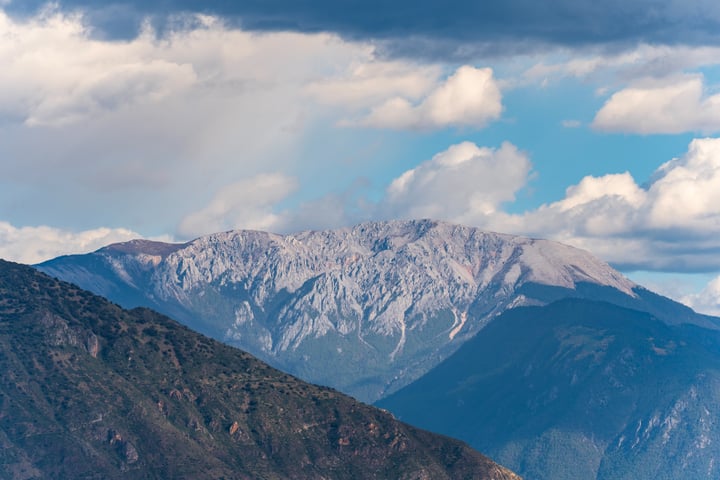 A majestic mountain range with snow-capped peaks and a blue sky with white clouds, with a small airplane flying in the foreground.