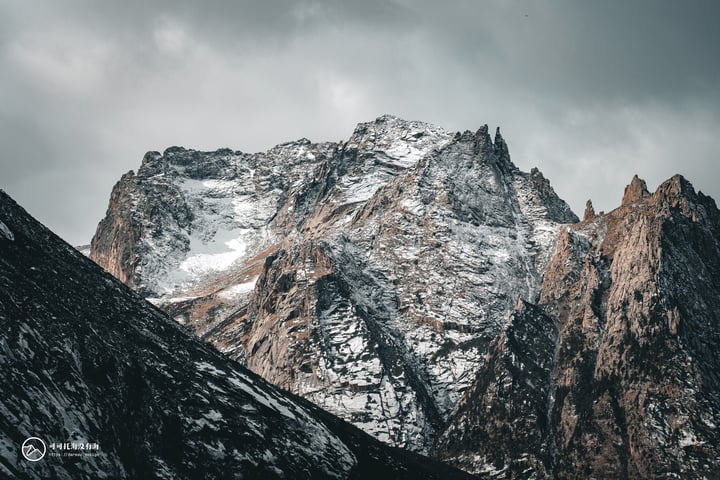 A majestic mountain range under a cloudy sky, with snow-covered peaks and rocky cliffs.