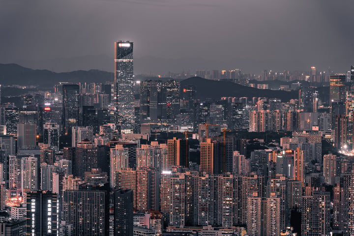 A nighttime cityscape features illuminated skyscrapers, a large Ferris wheel, and mountains in the background.