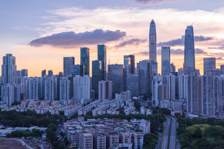 A city skyline at sunset, with tall buildings and a skyscraper in the background, a road running through the center, and a bridge in the foreground.