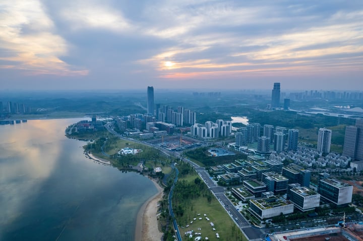 An aerial view of a city with tall buildings, a river, and a park, with a blue sky and clouds.