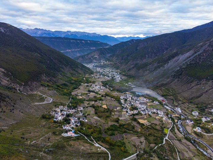 An aerial view of a small town nestled in a valley surrounded by mountains, with a winding river running through the valley. The town is surrounded by lush greenery and is nestled between the mountains.