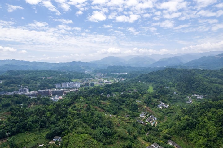An aerial view of a city nestled between mountains, with tall buildings and a large white dome in the center, surrounded by lush greenery.