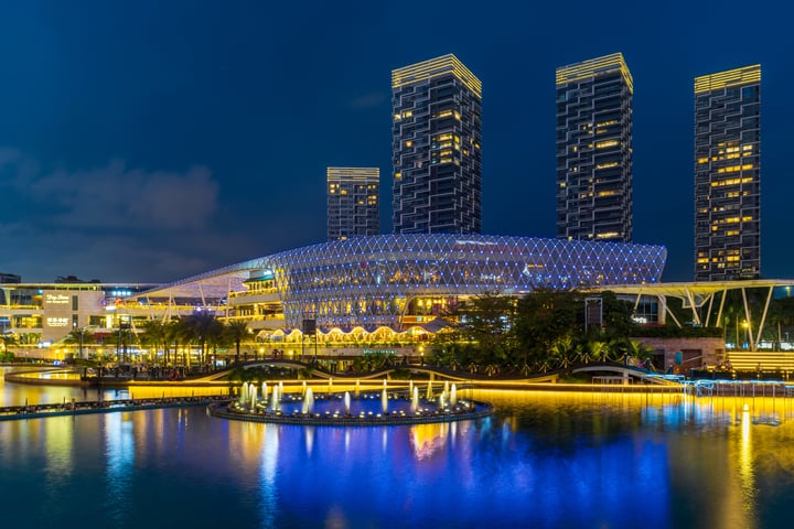 A modern, modern, modern building with three tall, curved towers and a curved roof is illuminated by blue lights against a dark blue sky. The building is situated near a body of water, with a bridge connecting the two. The image captures the building's reflection in the water, creating a beautiful mirror image.