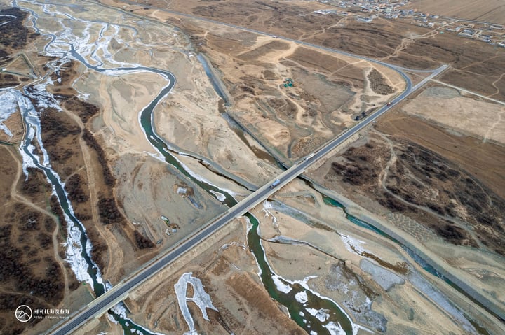 An aerial view of a rural area with a winding river, a road, and a small town in the distance.