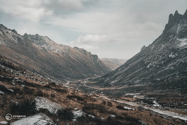 A mountainous valley with a winding river, rugged mountains, and a cloudy sky.