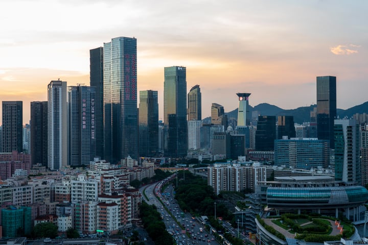 A cityscape with tall buildings, a busy highway, and mountains in the background.