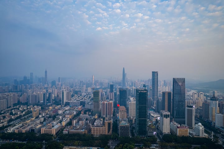 A panoramic view of a bustling cityscape with tall buildings, roads, and a hazy blue sky.