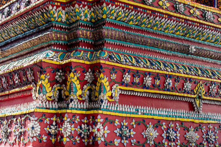 A close-up view of a temple's ornate, colorful facade showcases intricate floral patterns and intricate designs, with a vibrant red base and a rich, multicolored background.