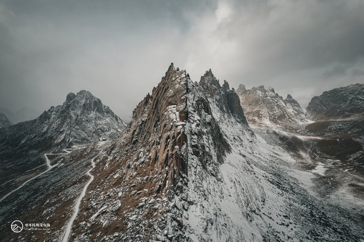 A snowy mountain range with a rocky peak and snow-covered peaks, surrounded by a cloudy sky.