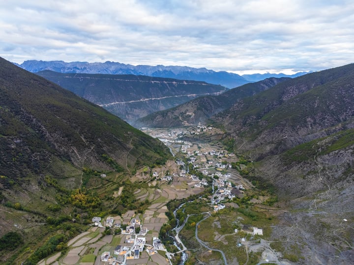 A small village nestled in a valley surrounded by mountains, with a winding river running through it.