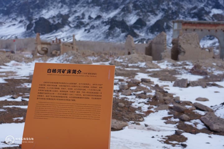 An orange sign with Chinese text stands in a snowy landscape, with a mountain range in the background.
