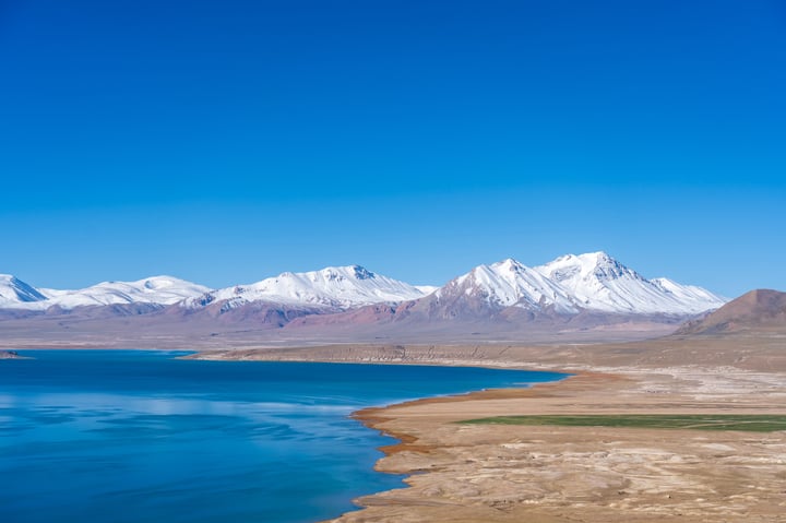 A breathtaking view of a mountain range with snow-capped peaks, a deep blue lake, and a vast expanse of sky.