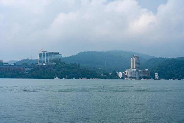 A cityscape with tall buildings, a mountain, and a lake with boats.