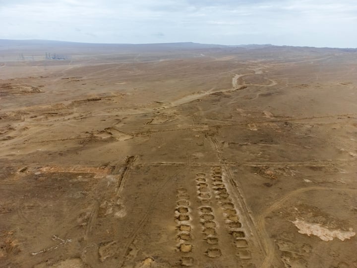 An aerial view of a vast, barren desert with a few scattered structures, including a circular structure and a circular building, surrounded by a vast expanse of sand and a few distant mountains.