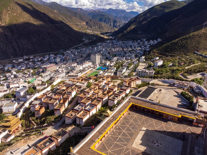 An aerial view of a mountainous valley with a large city, surrounded by lush green mountains, a large temple, and a large stadium.