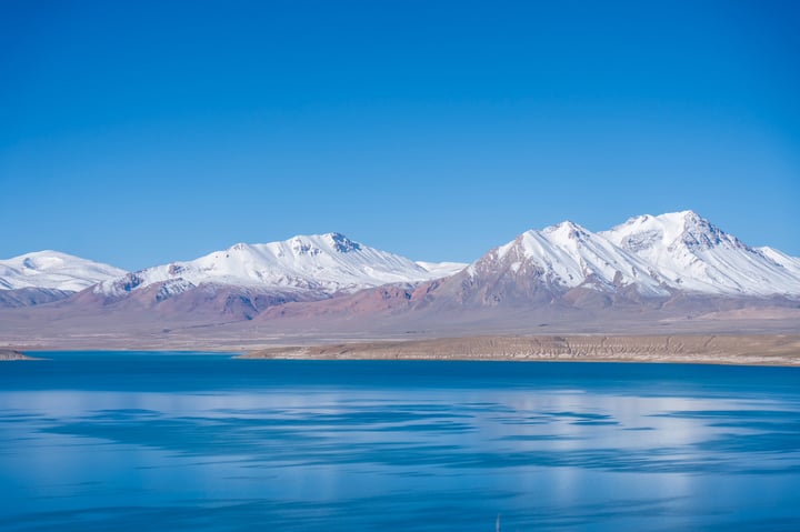 A breathtaking view of a mountain range with snow-capped peaks, a deep blue lake, and a vast expanse of sky.