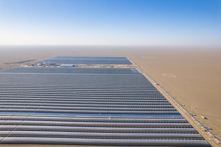 An aerial view of a large solar farm with rows of solar panels in a desert-like environment.