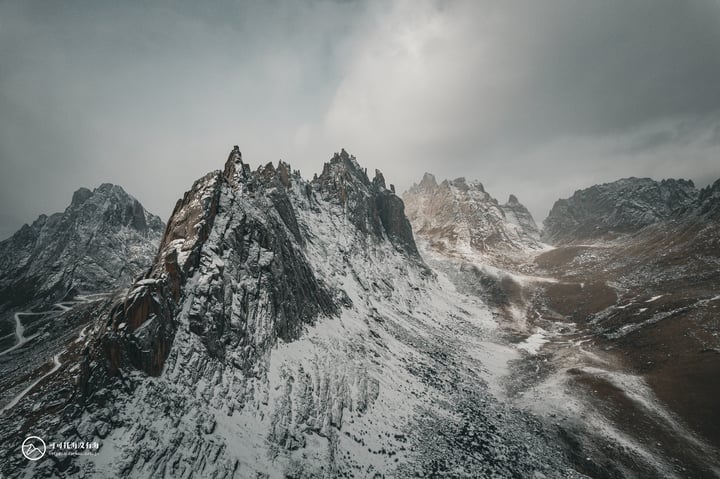 A snowy mountain range with jagged peaks and rocky cliffs, under a cloudy sky.