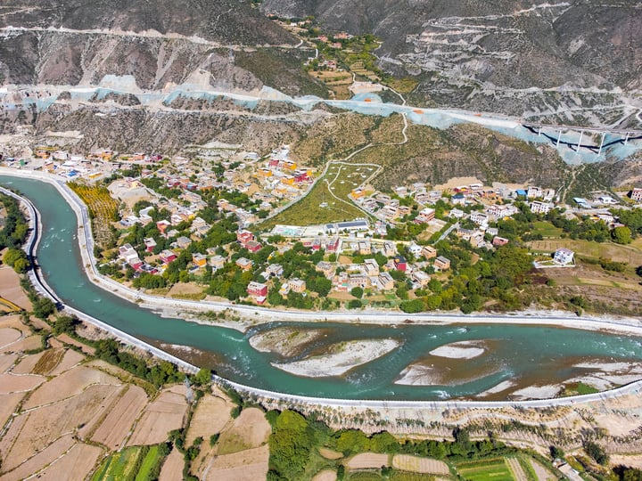 An aerial view of a picturesque valley with a winding river, surrounded by mountains and houses, showcasing a harmonious blend of nature and human habitation.