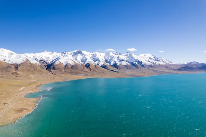A breathtaking view of a mountain range with snow-capped peaks, a deep blue lake, and a vast expanse of sky.