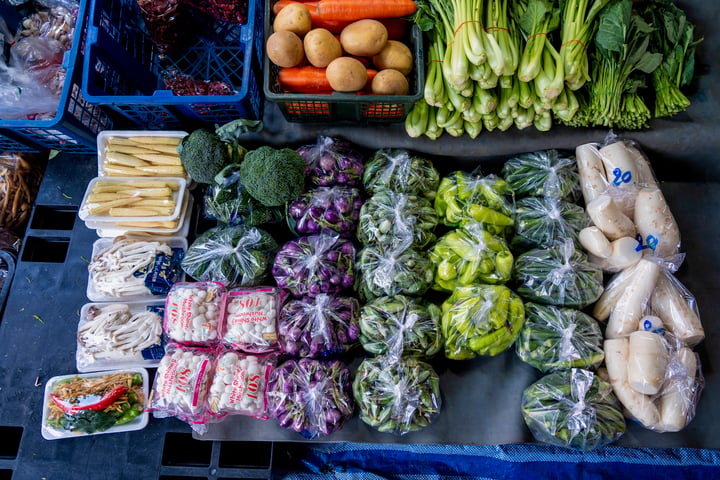A colorful display of fresh produce is displayed in a market stall, with carrots, broccoli, potatoes, and onions arranged neatly in clear plastic bags.