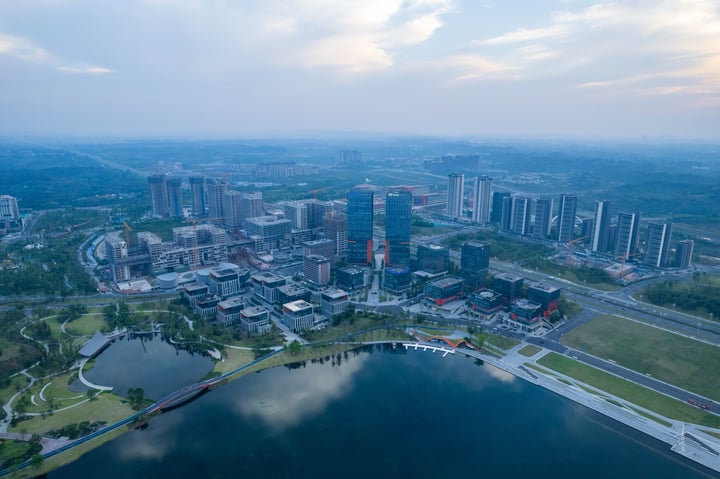 An aerial view of a city with tall buildings, a river, and a park, with a blue sky and clouds.