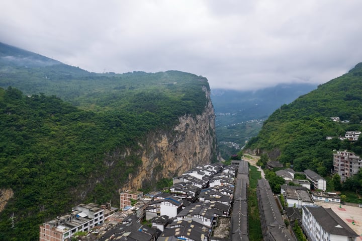 A mountainous valley with a steep cliff, surrounded by lush greenery, houses a road and a road sign. The sky is filled with clouds, and the valley is surrounded by mountains.
