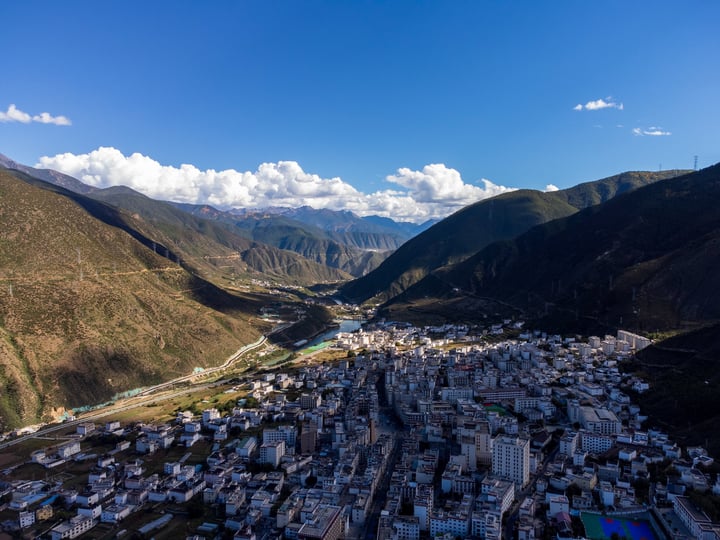 An aerial view of a mountainous city nestled between mountains, with a river flowing through the valley, surrounded by lush greenery.