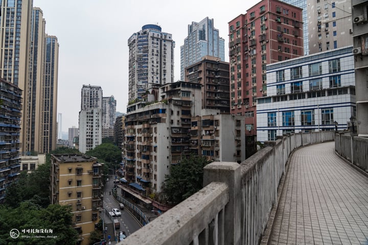 A cityscape with tall buildings, a walkway, and a street with cars and a bus.