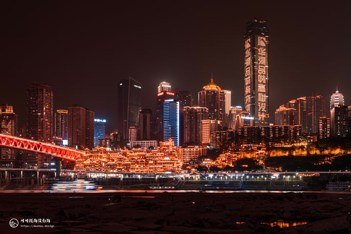 A nighttime cityscape features illuminated skyscrapers, a red bridge, and a river reflecting the city lights.