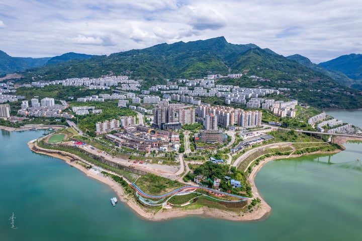 An aerial view of a city nestled between mountains, with a large body of water in the foreground and a cityscape in the background.
