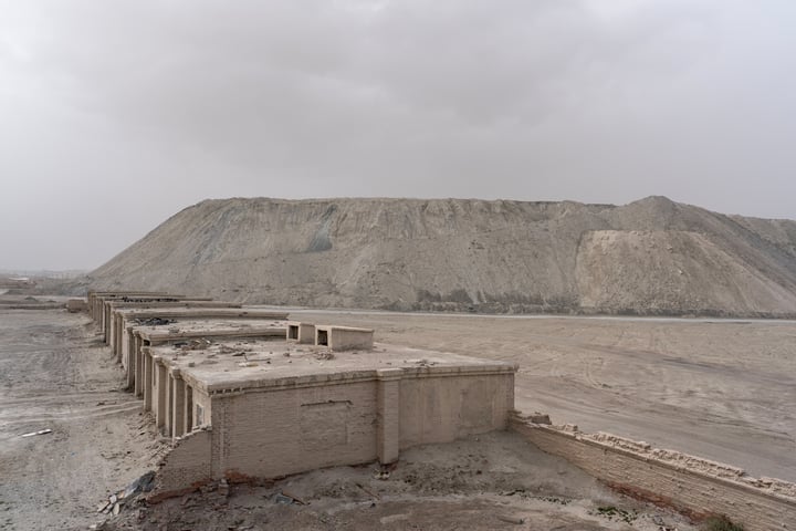 A desolate desert landscape with a large, rocky mountain in the background, a row of old, weathered buildings, and a cloudy sky.