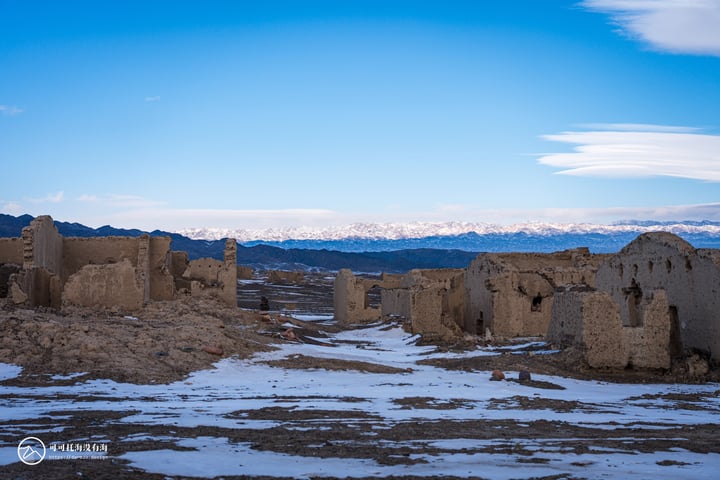 A desolate desert landscape with ruins, snow-covered mountains, and a clear blue sky.