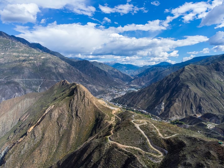 Aerial view of the Inca Trail in the Andes Mountains, with a blue sky and clouds, showcasing the rugged terrain and winding road.