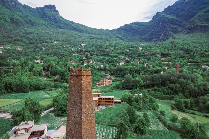 A serene mountainous landscape with a brick tower, a cluster of buildings, and a field of green vegetation.
