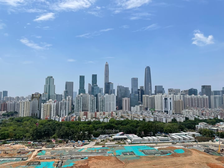 A city skyline with tall buildings under a clear blue sky, with a construction site in the foreground.
