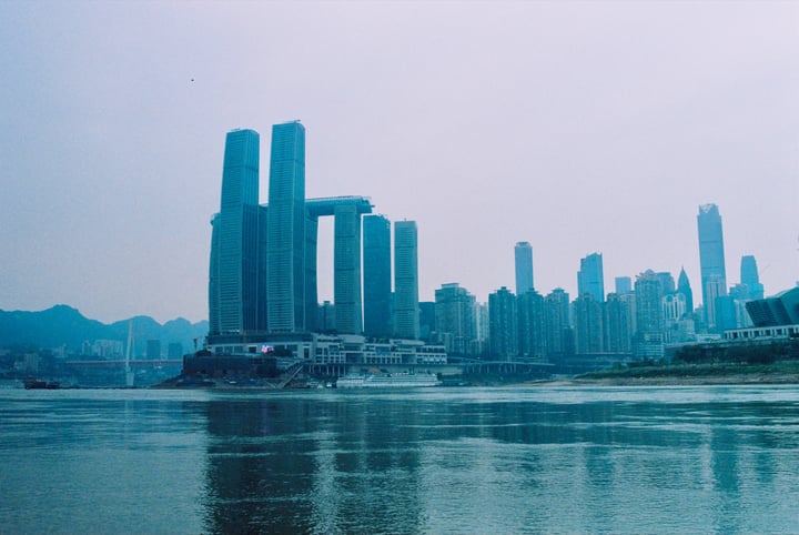 A cityscape with tall buildings, a large body of water, and a boat on the water.