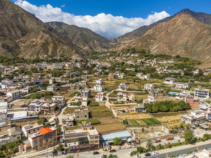 A serene mountain town with white buildings, green fields, and a clear blue sky.
