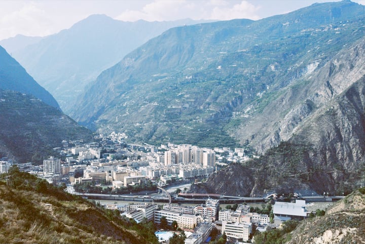 A city nestled in a valley, surrounded by mountains and a river, with a clear blue sky above.