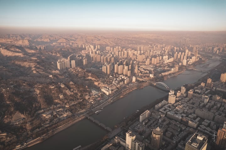 An aerial view of a bustling city with tall buildings, a river, and bridges, all set against a clear blue sky.