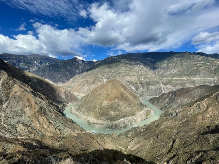 A breathtaking view of a valley with a river winding through it, surrounded by mountains and a blue sky with clouds.