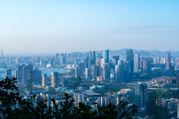 A cityscape with tall buildings, a river, and mountains in the background, captured from a high vantage point.