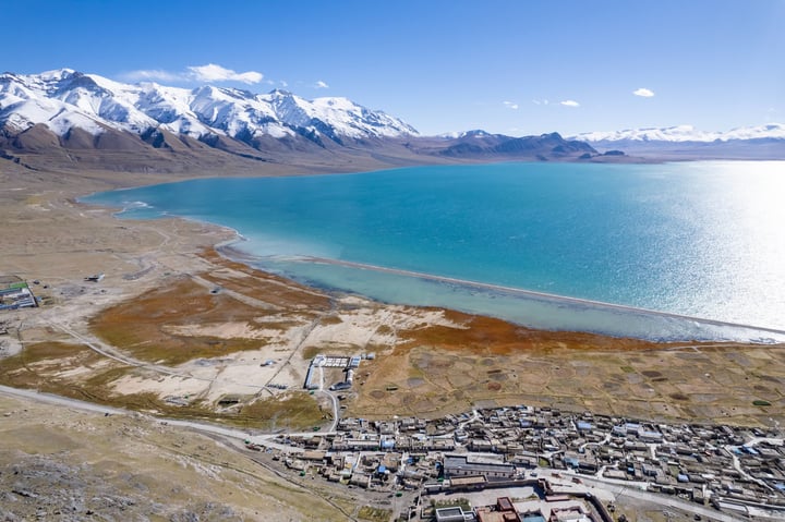 A breathtaking view of a mountain range with snow-capped peaks, a deep blue lake, and a vast expanse of sky.