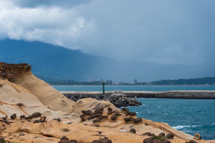 A coastal landscape with a rocky shoreline, a lighthouse, and a mountain range in the background.