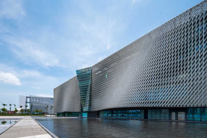 A modern building with a geometric facade and large glass windows is situated in a cityscape. The building's unique design and modern architecture make it a prominent landmark.