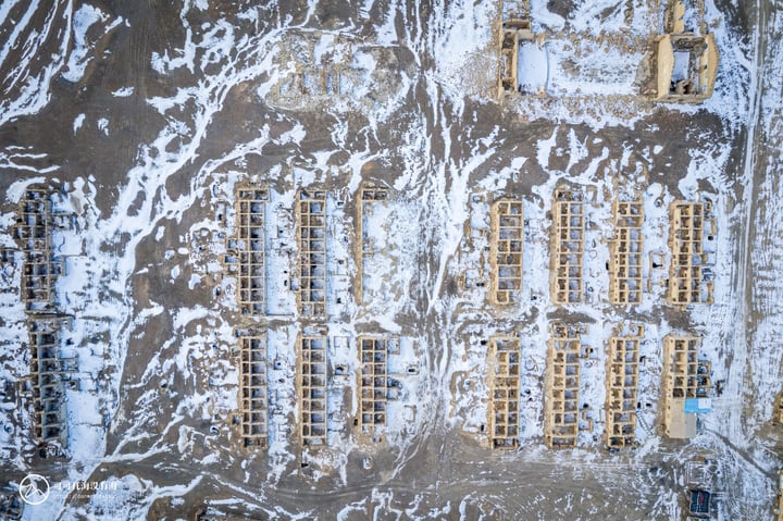 An aerial view of a construction site with numerous wooden structures, some with windows, covered in snow.