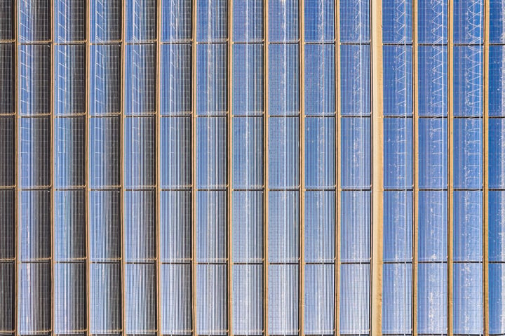 An aerial view of a large solar farm with rows of solar panels in a desert-like environment.